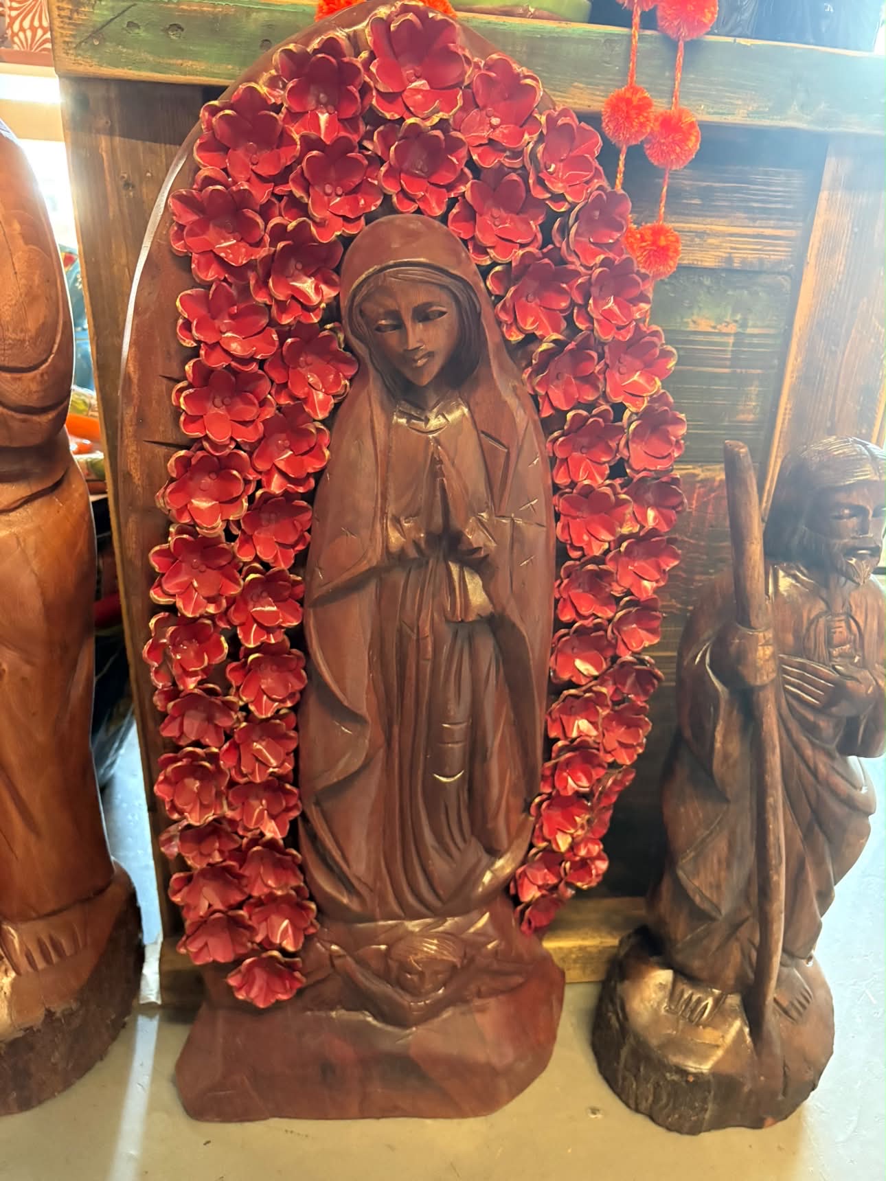 Wooden Guadalupe sculpture surrounded by red paper flowers